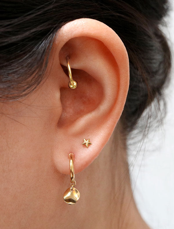 gold hoop earring with wavy coin charm modelled