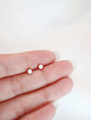 tiny opal stud earrings held in hand